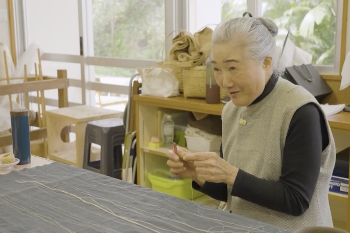 おしゃべりしながらも手は滑らかに動き、苧績み（うーうみ・取りためた繊維を裂き、一本の糸にする作業）をする、会長の津波洋子さん